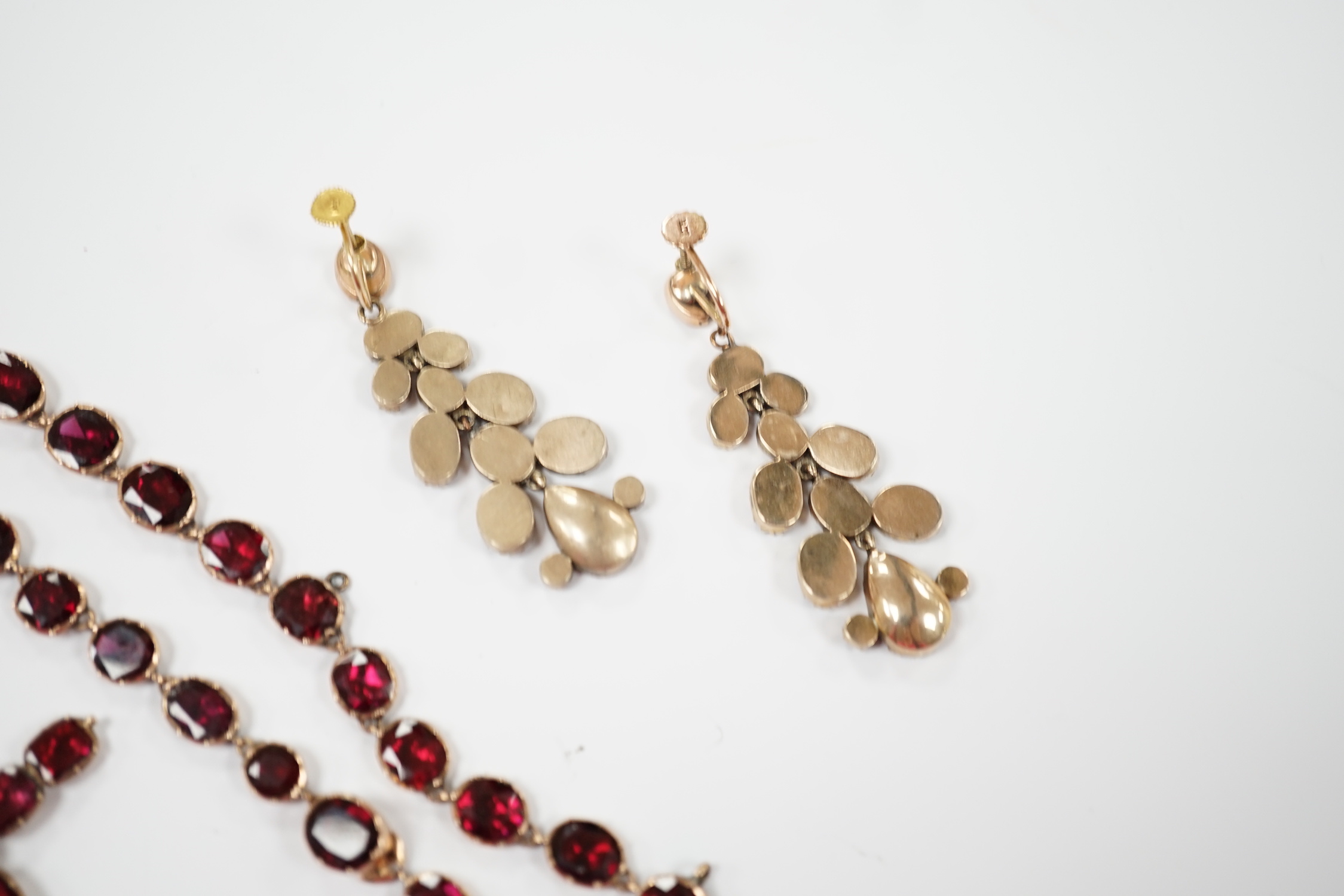 Six items of Victorian oval cut garnet set jewellery, including a yellow metal necklace (lacking drops?), 37cm, a pair of 9ct ear clips, a yellow metal cross pendant with cushion cut stones, gross weight 30 grams and a p